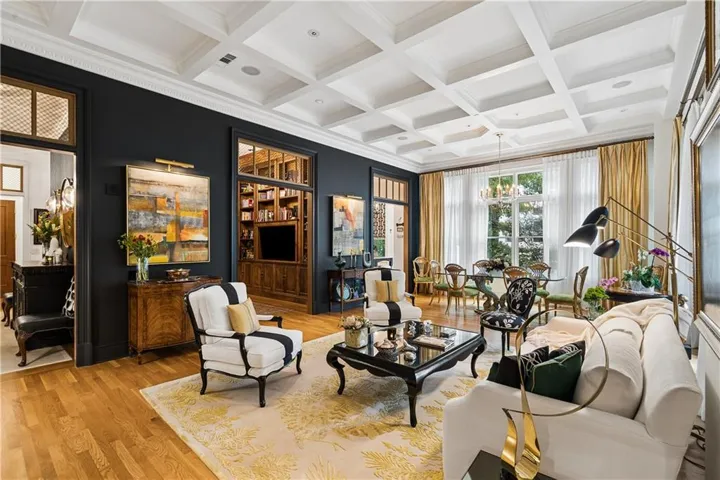 Hardwood flooring throughout, coffered ceiling, built-in shelving, large windows with full-length drapery, and a chandelier