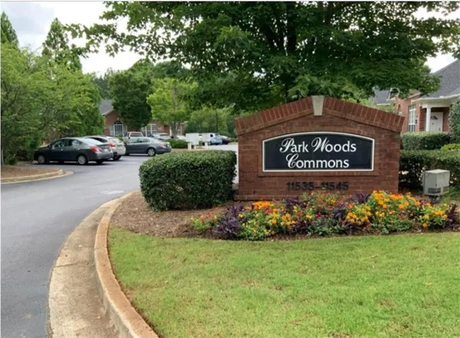 Brick monument sign with integrated lettering, set amid landscaped grounds, featuring mature trees and a paved parking area