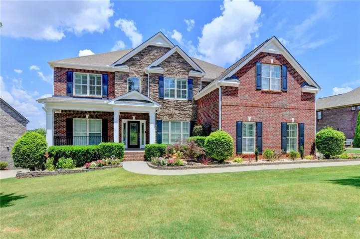 Traditional brick and stone exterior featuring a covered entry, established landscaping, and a manicured lawn