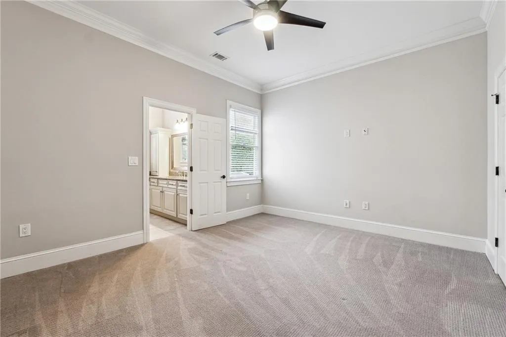 Unfurnished bedroom featuring ornamental molding, light colored carpet, ceiling fan, and ensuite bath