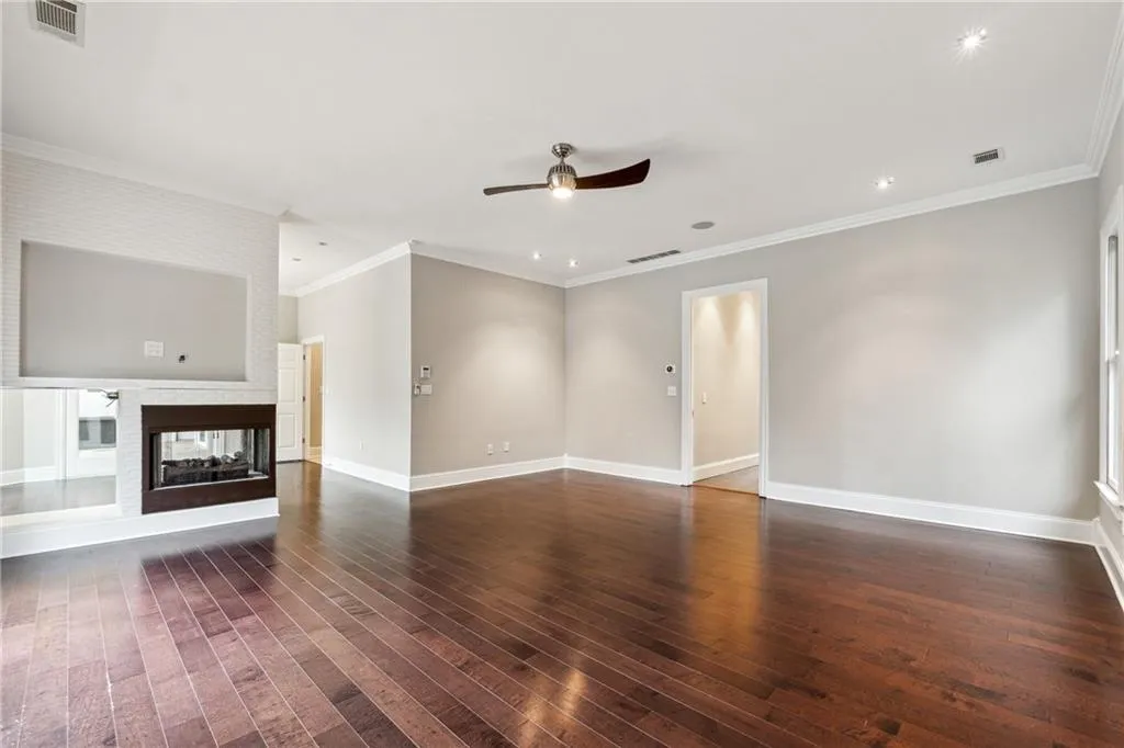 Unfurnished living room with a multi sided fireplace, dark hardwood / wood-style floors, crown molding, and ceiling fan