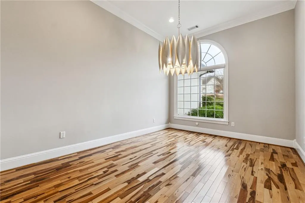 Unfurnished dining area with wood-type flooring, a notable chandelier, and crown molding