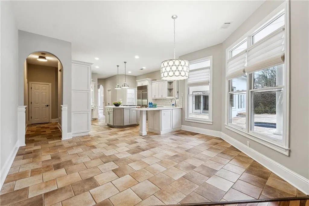 Kitchen with a kitchen bar, built in fridge, an island with sink, pendant lighting, and white cabinets