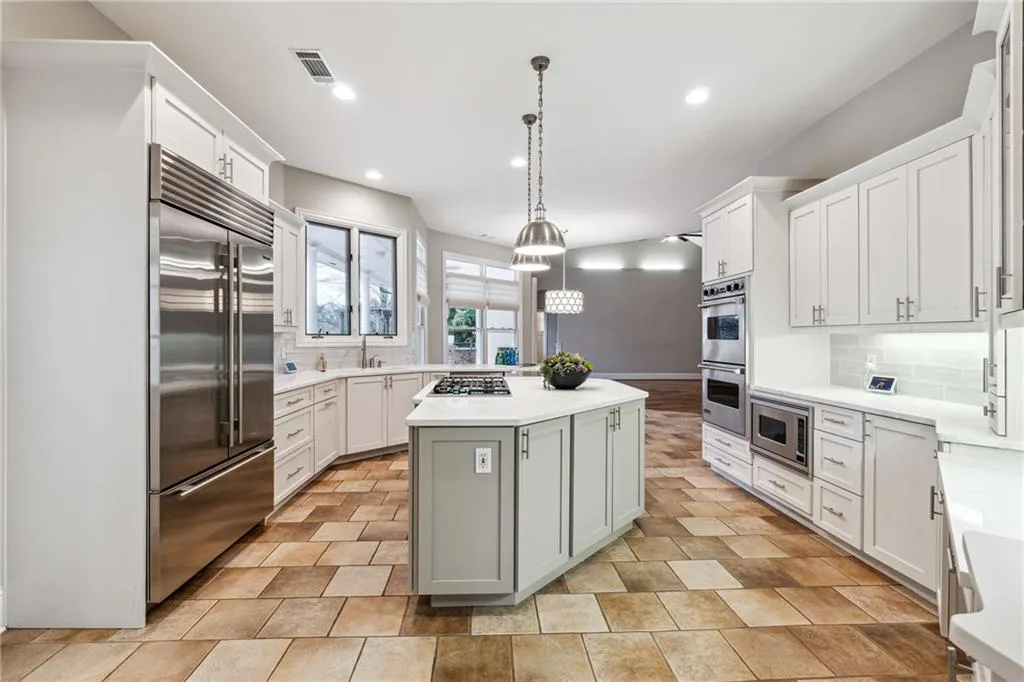 Kitchen featuring white cabinetry, decorative light fixtures, built in appliances, a center island, and backsplash