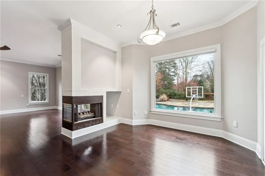Unfurnished living room featuring a multi sided fireplace, dark wood-type flooring, and crown molding