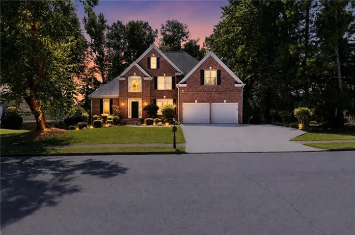 Brick exterior with a gabled roofline, mature trees, a two-car garage, and a concrete driveway