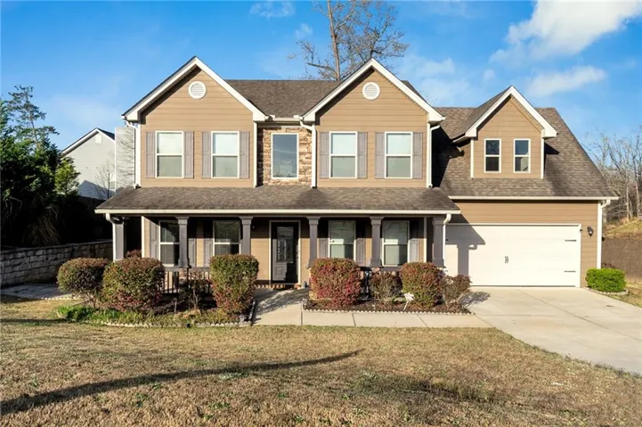 Two-story residence featuring a two-car garage, stone and siding exterior, covered porch with columns, a prominent front gable, and a concrete driveway