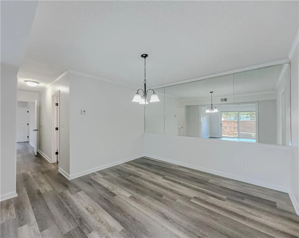 Unfurnished dining area featuring wood finished floors, ornamental molding, baseboards, visible vents, and a notable chandelier