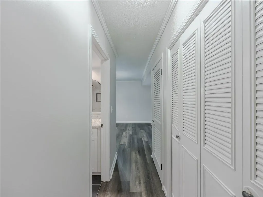 Hallway with ornamental molding, a textured ceiling, dark wood finished floors, arched walkways, and baseboards