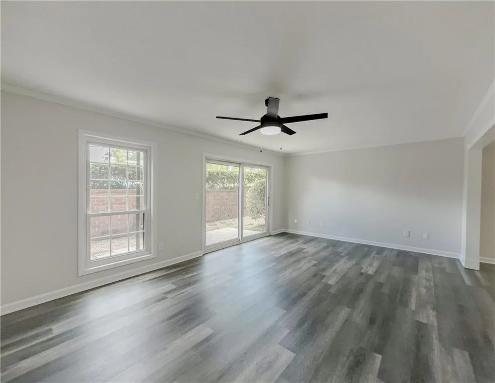 Spare room featuring crown molding, ceiling fan, baseboards, and dark wood-style floors