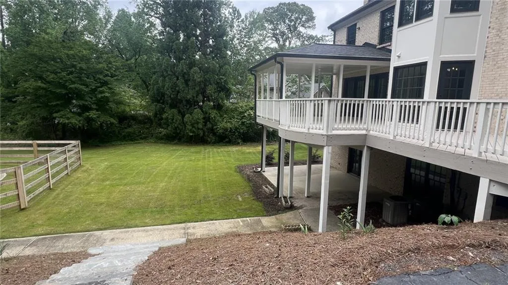 View of green lawn with a wooden deck and a patio area