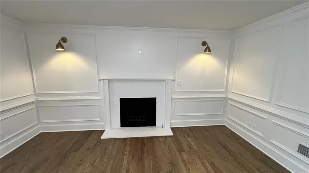 Unfurnished living room featuring a decorative wall, dark wood-style flooring, a brick fireplace, and crown molding