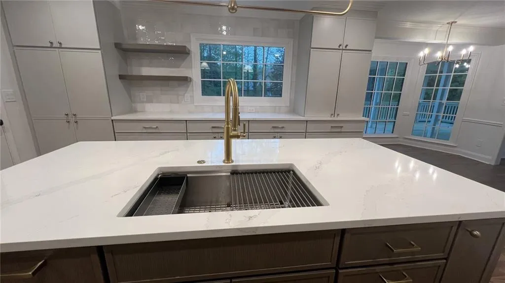 Kitchen featuring ornamental molding, backsplash, light stone countertops, a chandelier, and an island with sink