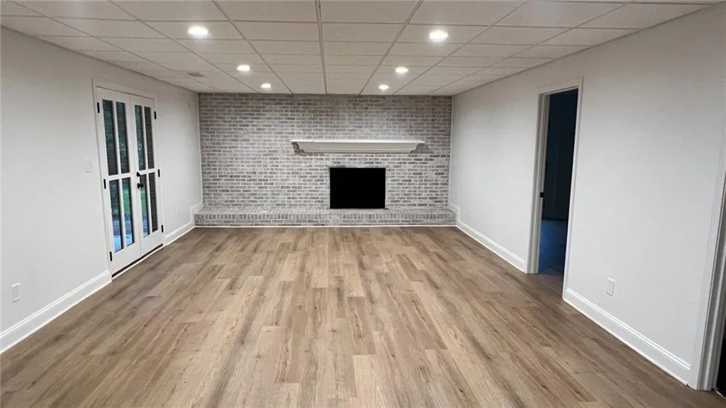 Unfurnished living room with recessed lighting, a drop ceiling, wood finished floors, a brick fireplace, and brick wall