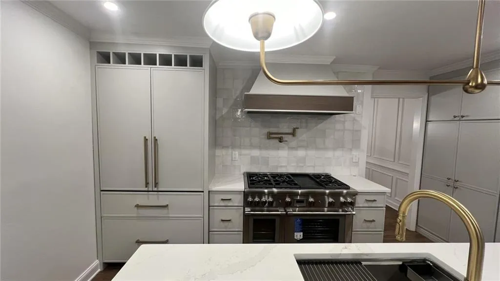 Kitchen featuring crown molding, double oven range, decorative backsplash, range hood, and light stone counters