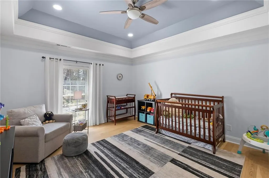 Bedroom with a crib, light wood-type flooring, a tray ceiling, recessed lighting, and ceiling fan
