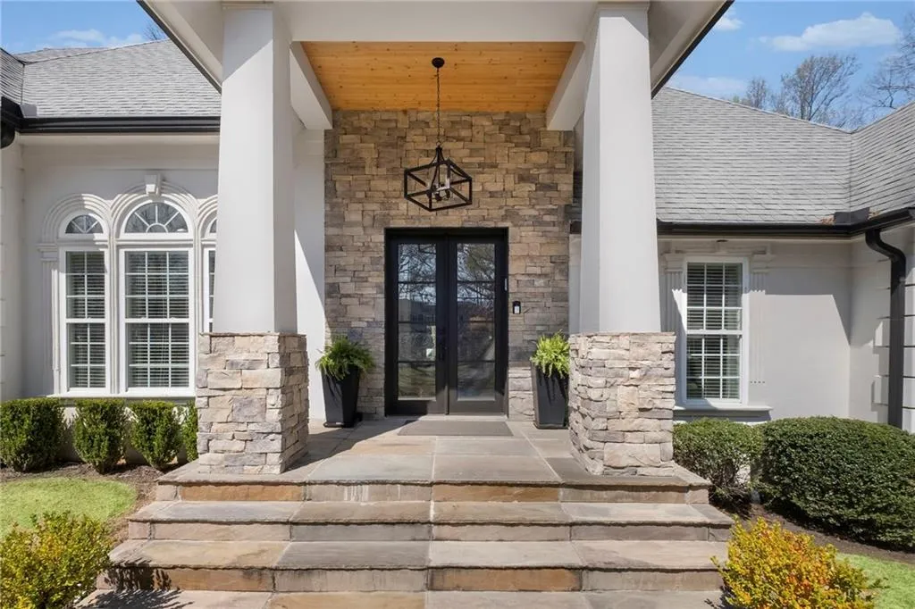 Property entrance featuring french doors, stone siding, a shingled roof, covered porch, and stucco siding