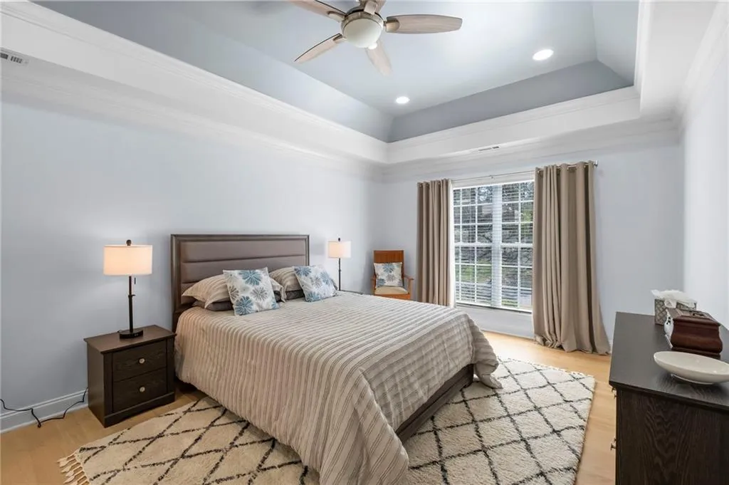 Bedroom featuring light wood finished floors, recessed lighting, a ceiling fan, ornamental molding, and a tray ceiling