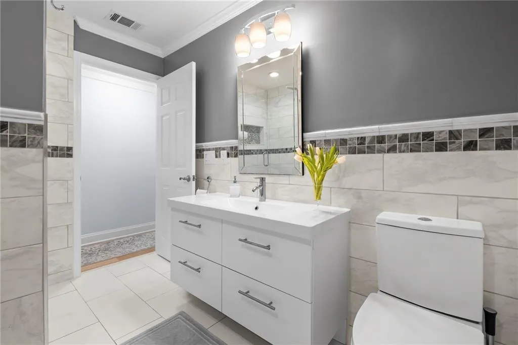 Full bath featuring tile walls, vanity, ornamental molding, wainscoting, and light tile patterned floors