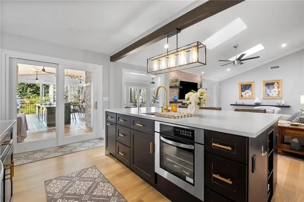 Kitchen featuring open floor plan, ceiling fan, a kitchen island with sink, oven, and decorative light fixtures