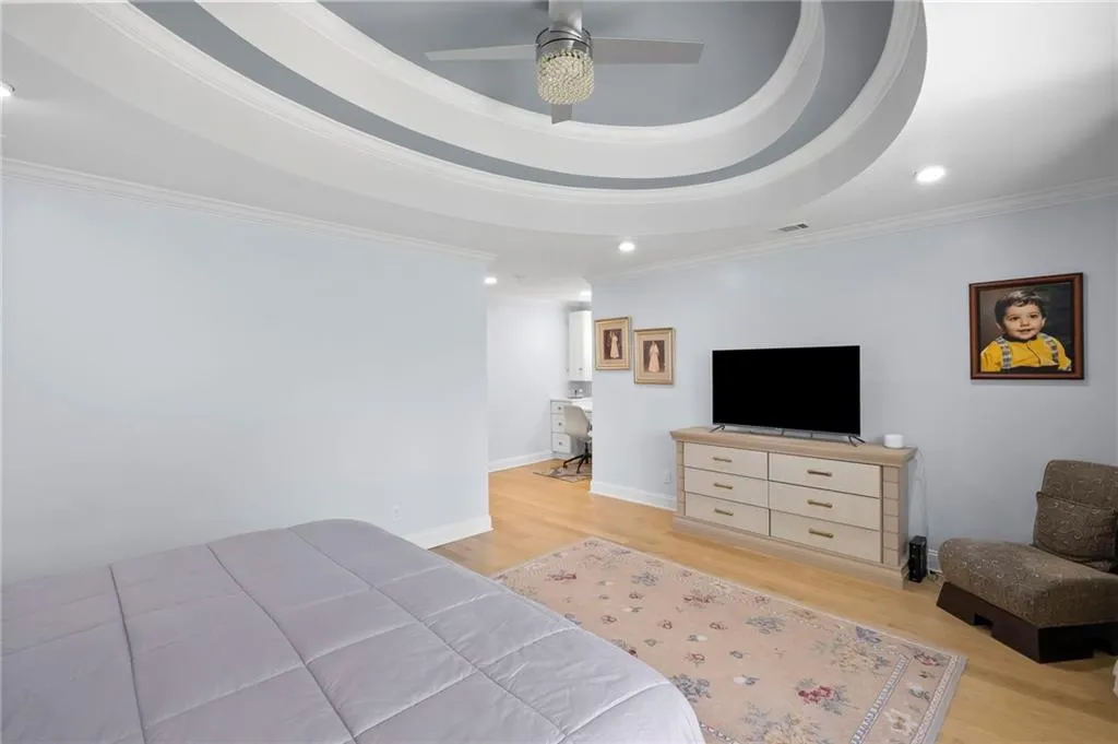Bedroom with recessed lighting, light wood-type flooring, a ceiling fan, ornamental molding, and a raised ceiling