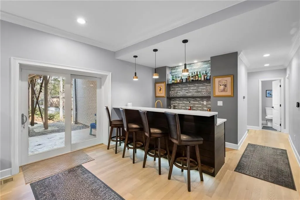 Indoor wet bar with ornamental molding, pendant lighting, and light wood finished floors