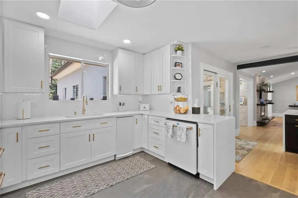 Kitchen with open shelves, a peninsula, dishwasher, light stone countertops, and white cabinets