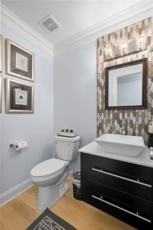 Half bathroom featuring ornamental molding, vanity, light wood finished floors, and decorative backsplash