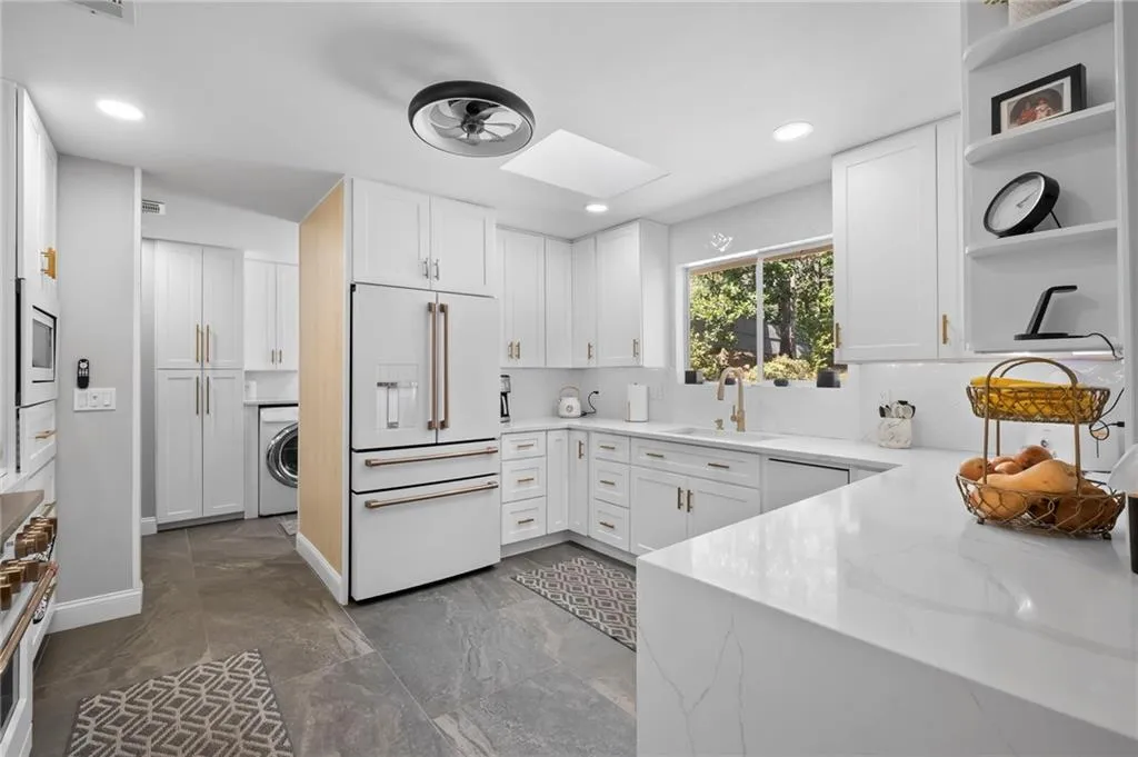 Kitchen with high end white fridge, a skylight, white cabinetry, light stone countertops, and open shelves
