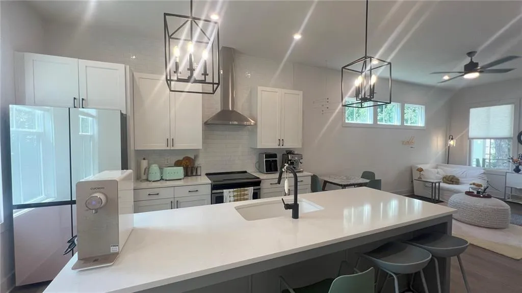 Kitchen with tasteful backsplash, range hood, a chandelier, range with electric cooktop, and white cabinetry