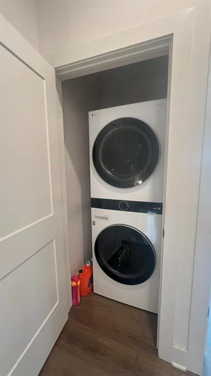 Laundry room with dark wood finished floors and stacked washer / drying machine