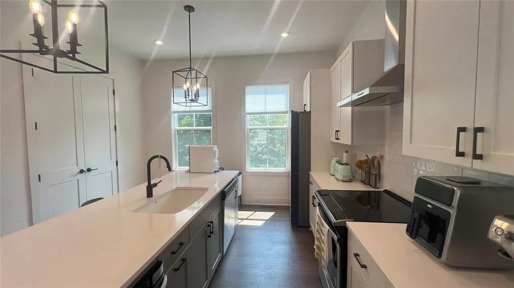 Kitchen with stainless steel appliances, wall chimney range hood, a chandelier, white cabinets, and decorative light fixtures
