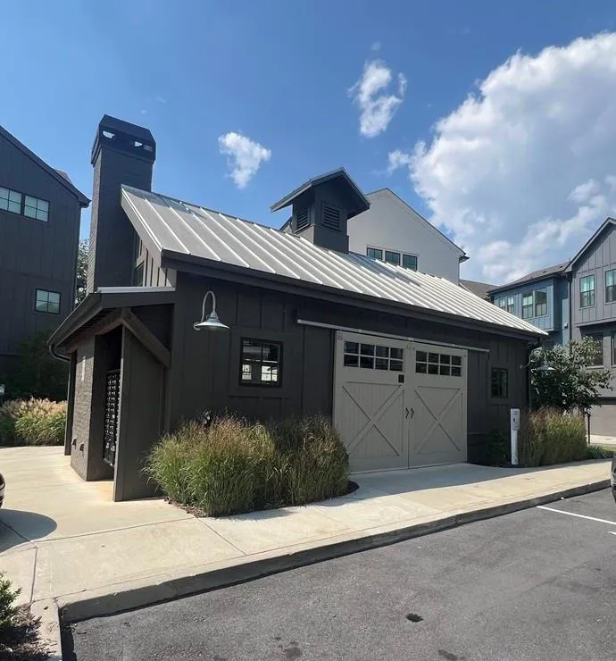 View of front facade with board and batten siding, a standing seam roof, a metal roof, a garage, and a chimney