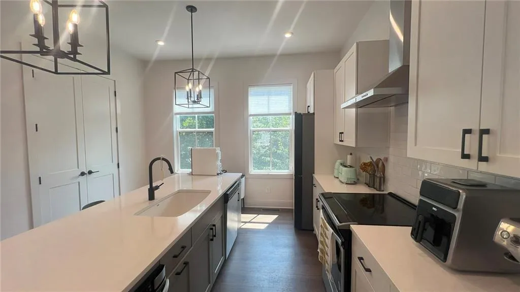 Kitchen featuring appliances with stainless steel finishes, wall chimney exhaust hood, a chandelier, pendant lighting, and white cabinetry