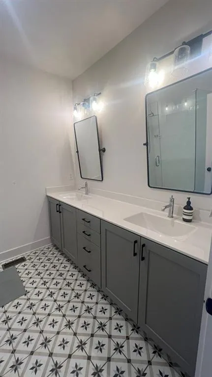 Bathroom featuring a shower stall, double vanity, and light floors