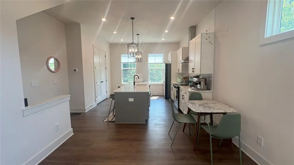Kitchen with white cabinetry, a kitchen island with sink, hanging light fixtures, dark wood-type flooring, and a kitchen breakfast bar