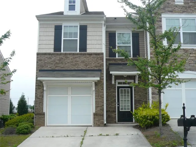Brick and stone Colonial featuring a two-car garage with white panel doors, black shutters, and a covered front entry