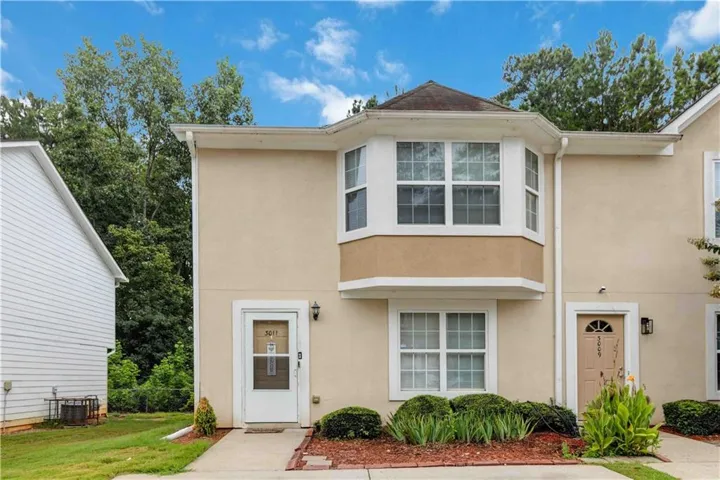 Stucco exterior featuring a bay window, white window frames, and decorative landscaping