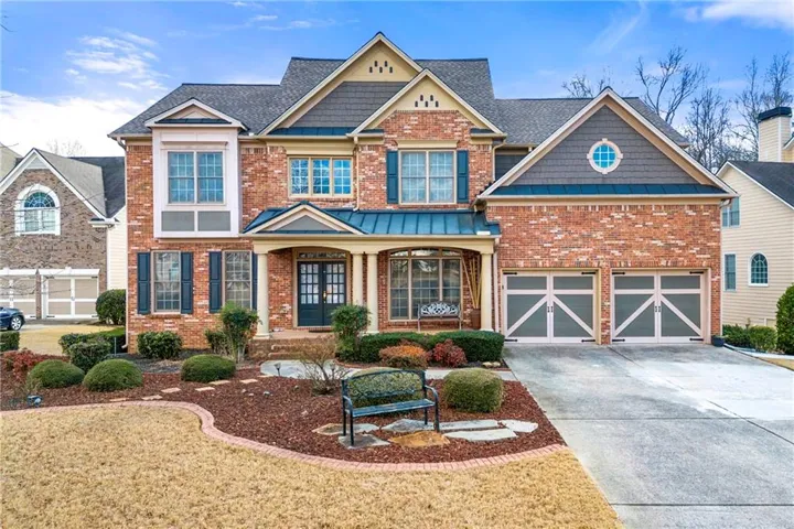 Brick exterior with stone accents, a covered front porch, a multi-car garage, and established landscaping