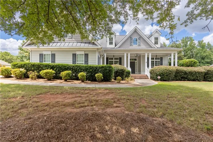 Front exterior featuring dormer windows, a covered porch with white columns, light gray siding, and dark shutters