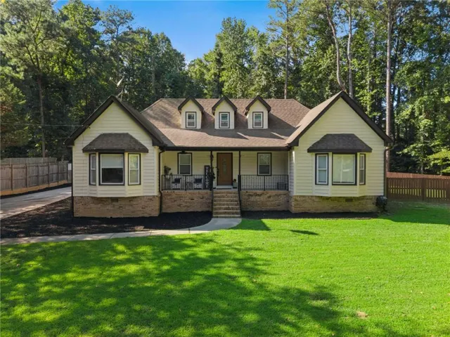 Light-colored siding exterior with a brown shingle roof, complemented by a covered front porch featuring black railings