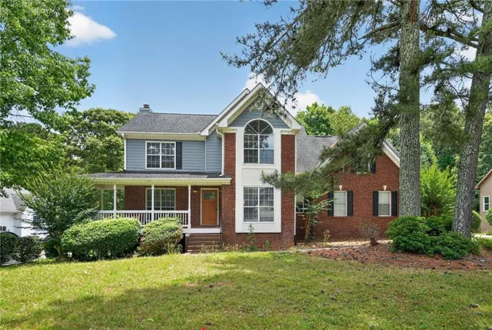 Two-story residence featuring a brick and siding facade, covered front porch, arched window, and mature landscaping