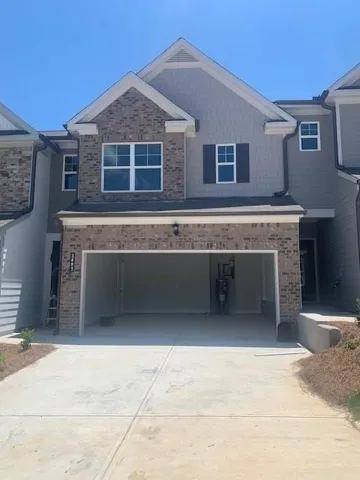 Two-story townhouse with a brick and siding facade, featuring a two-car garage, multiple windows with white trim, and dark functional shutters on the upper level
