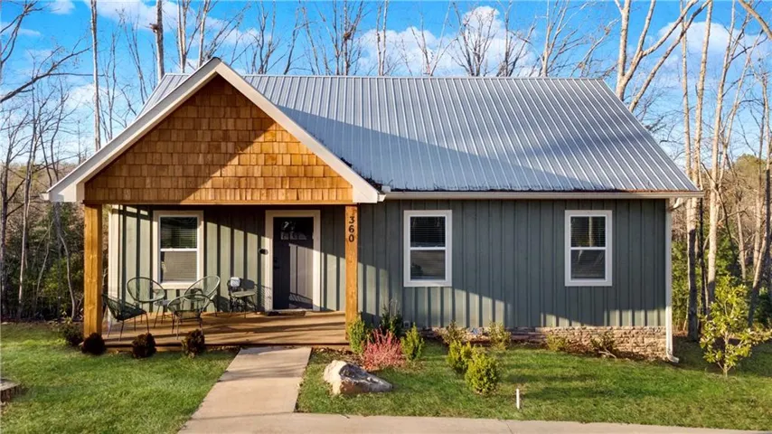 Board and batten siding, metal roof, wood shake gables, covered porch, and well-maintained landscaping