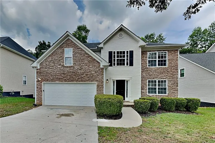 Two-story dwelling with a stone and siding exterior, featuring a two-car garage, established front landscaping, and a concrete driveway