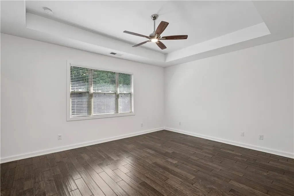 Empty room featuring a raised ceiling, dark wood-type flooring, and a ceiling fan