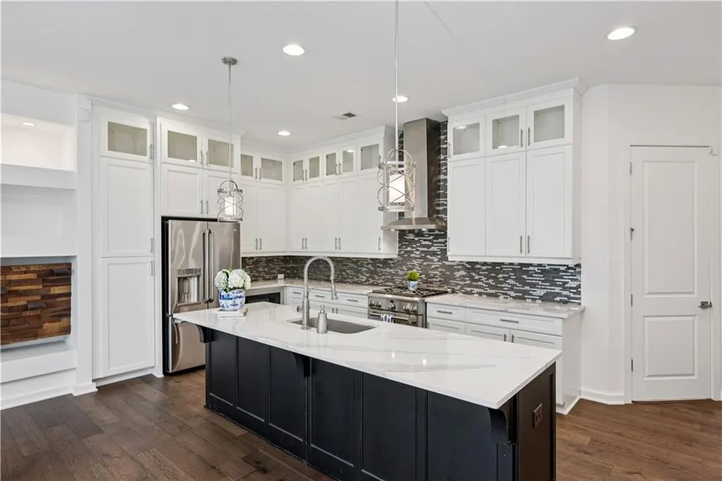 Kitchen with white cabinets, high end appliances, light stone counters, dark wood finished floors, and wall chimney range hood