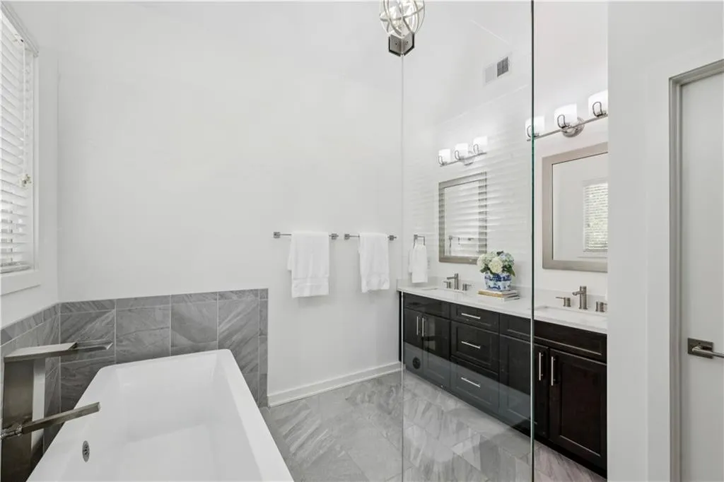 Full bath featuring a soaking tub, double vanity, and light marble finish flooring