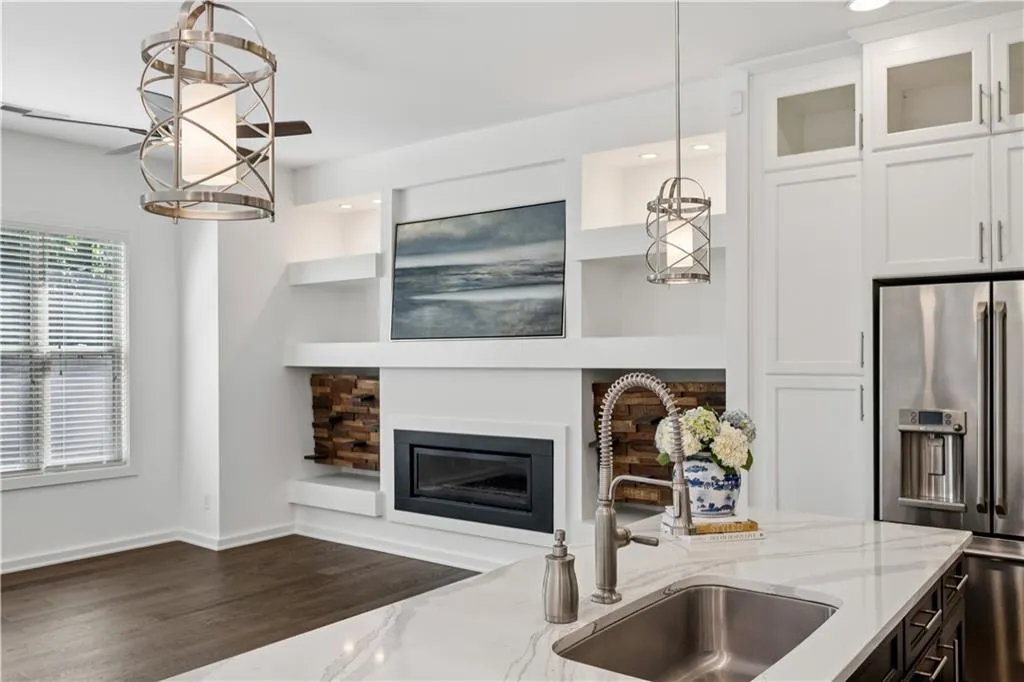 Kitchen featuring stainless steel refrigerator with ice dispenser, light stone countertops, hanging light fixtures, white cabinets, and recessed lighting