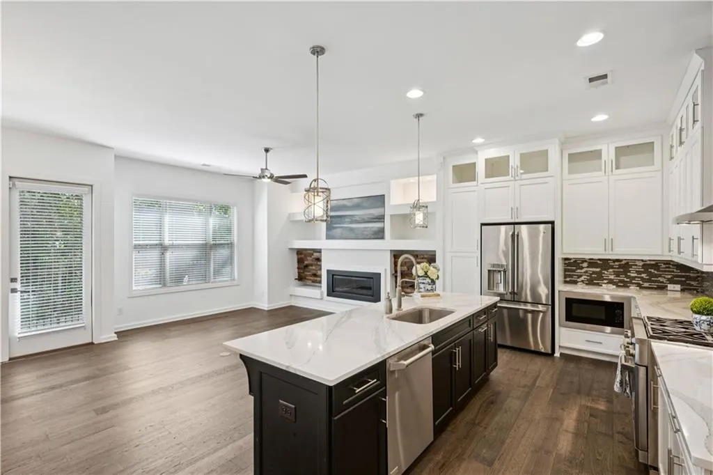 Kitchen featuring stainless steel appliances, white cabinetry, backsplash, light stone countertops, and decorative light fixtures
